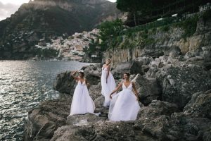 Women in white dresses on the rocks to greet guest for Midsummer Night's Eve-themed white welcome party at this Positano wedding weekend in Villa Tre Ville | Photo by Gianni di Natale