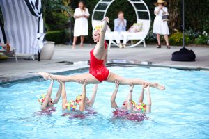 Synchronized swimmer doing a split in red suit and colorful cap at this South Beach-inspired first birthday pool party in the Hamptons | Photo by Cava Photo