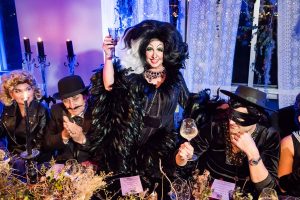 Cruella de Vil, seated with Zorro, a man in a bowler hat, and Sandy from Grease, making a toast at this epic halloween party at The Standard in NYC | Photo by Gruber Photographers