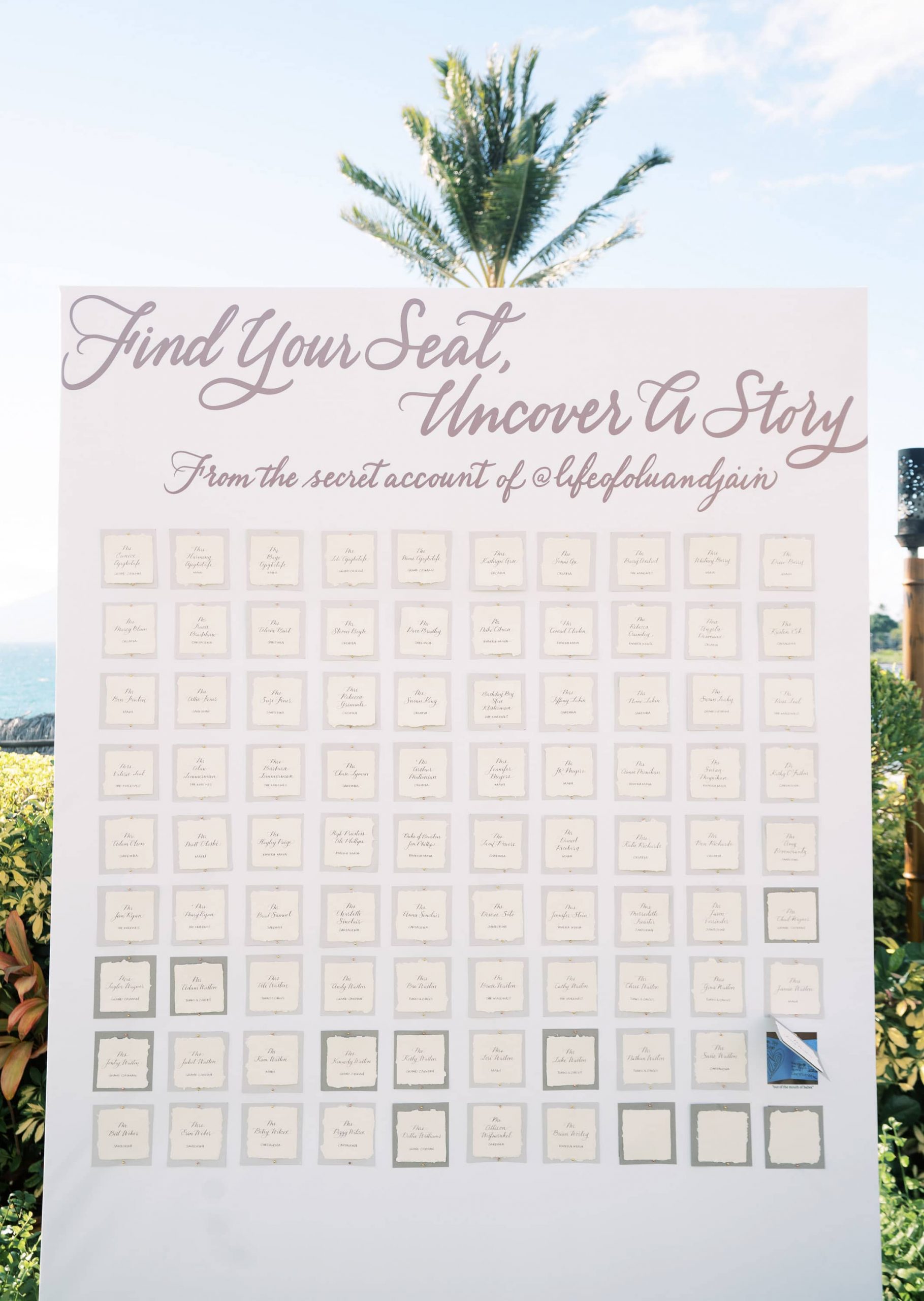 Peel away seating chart at Maui wedding at Four Seasons Resort Maui in Wailea, Hawaii | Photo by James x Schulze, text says "Find your Seat, Uncover a Story from the secret account of @lifeofoluanandjain