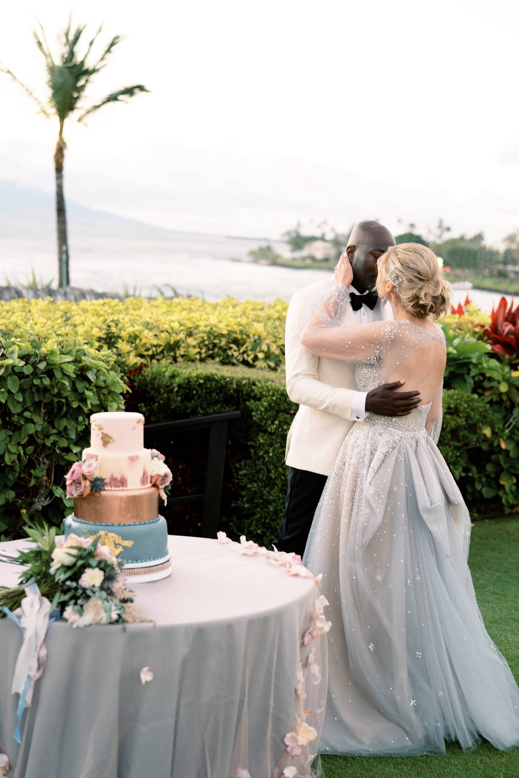 Bride and groom kiss in front of wedding cake at Maui wedding at Four Seasons Resort Maui in Wailea, Hawaii | Photo by James x Schulze
